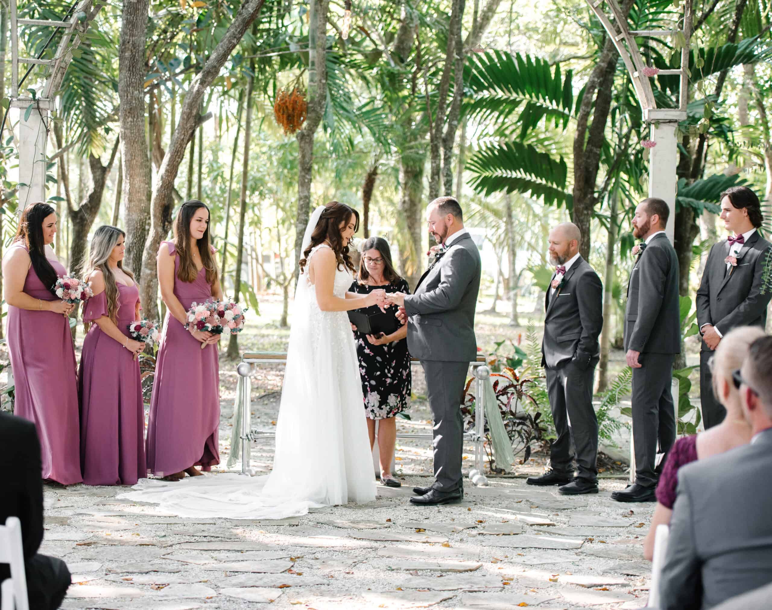 Couple getting married outdoors in a tropical garden setting with brides maids and grooms men.